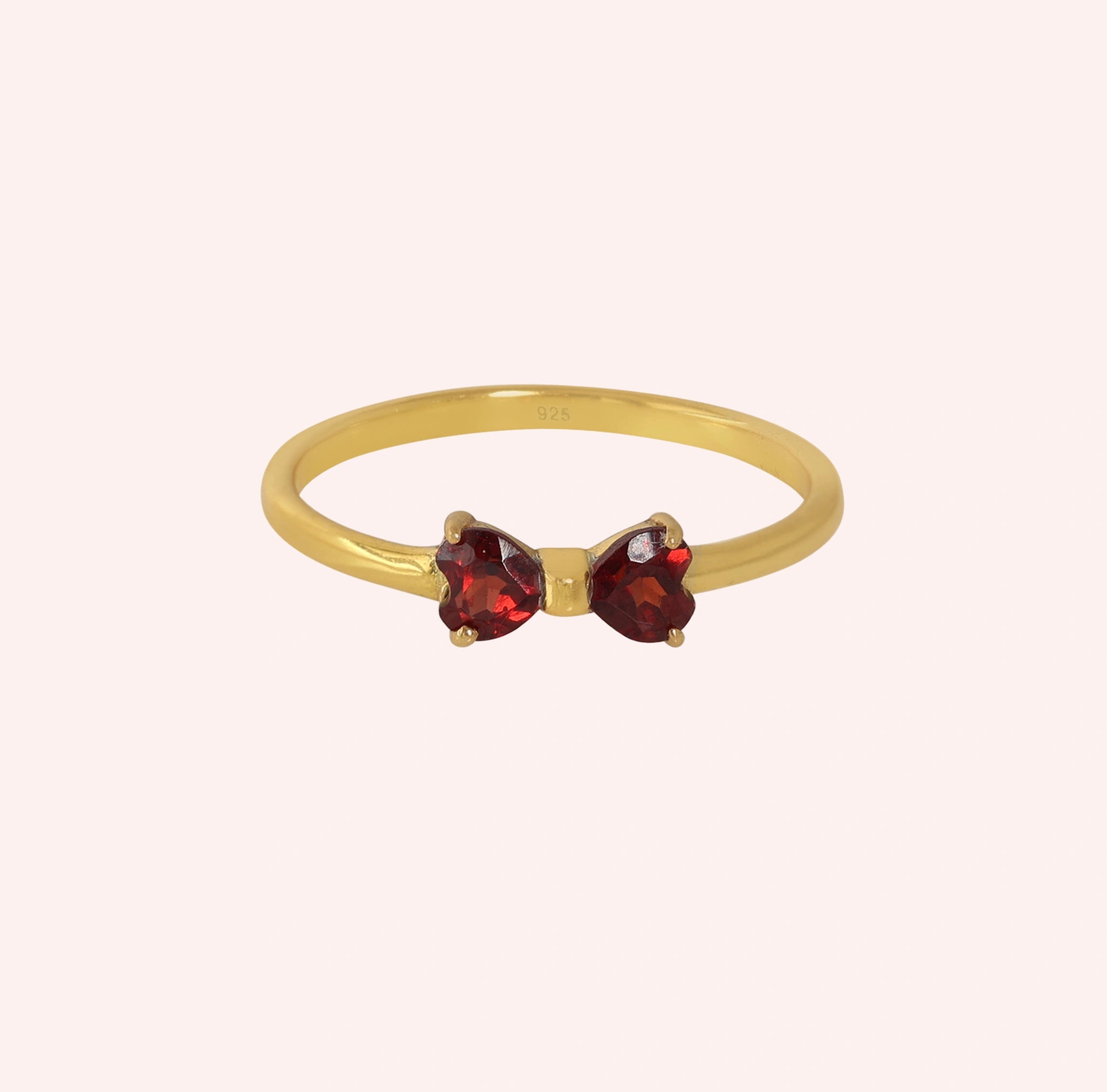 Bow_ring_close_up_front_angle_shot_gold_plated_silver_band_red_heart_garnet_gemstones_on_solid_pink_background