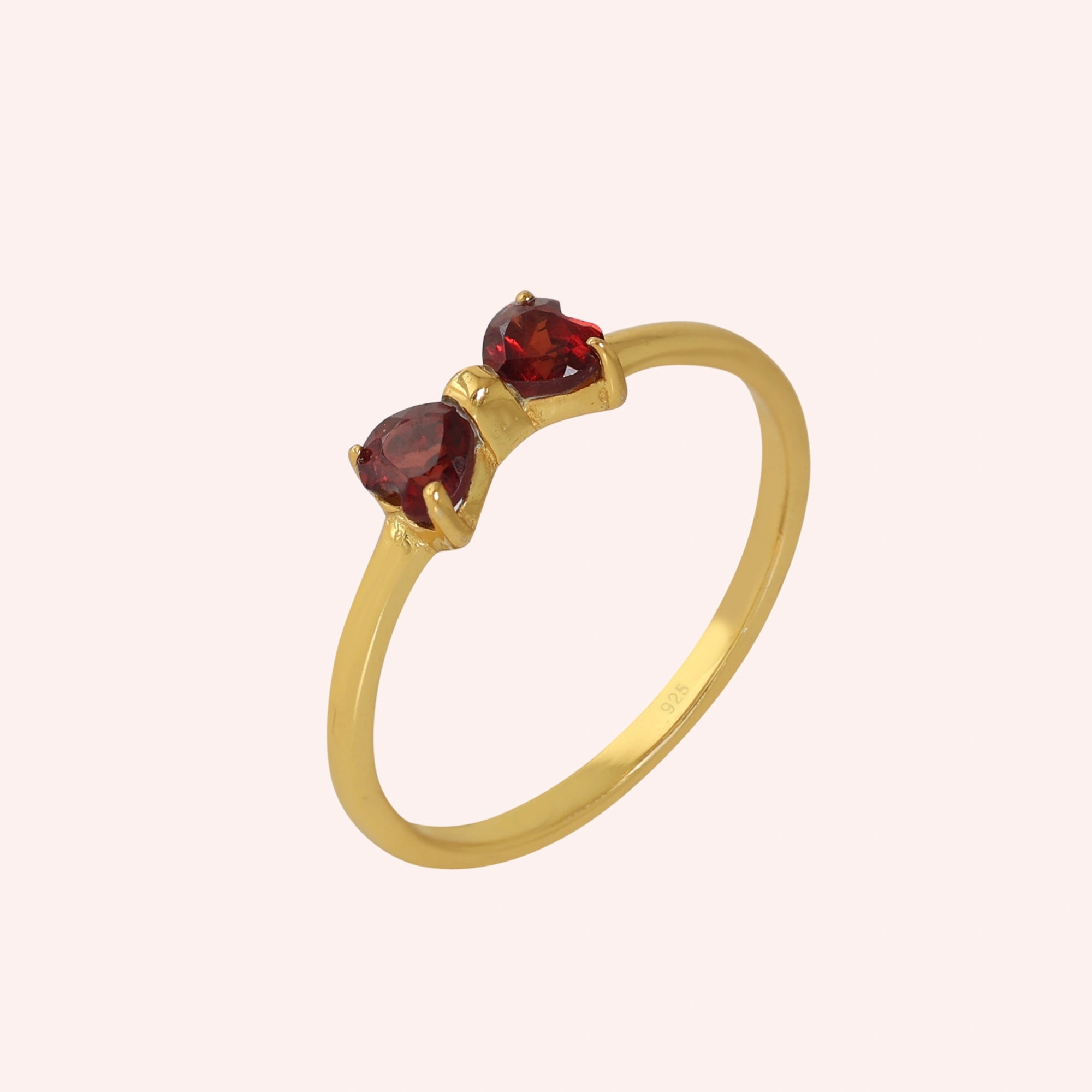 Bow_ring_close_up_slightly_angled_shot_gold_plated_silver_band_red_heart_garnet_gemstones_on_solid_pink_background