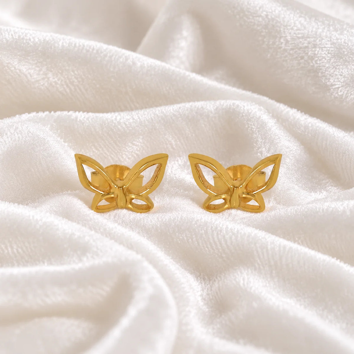 Butterfly_earrings_in_gold_plated_silver_in_a_stud_design_at_front_angle_view_on_soft_fabric_background