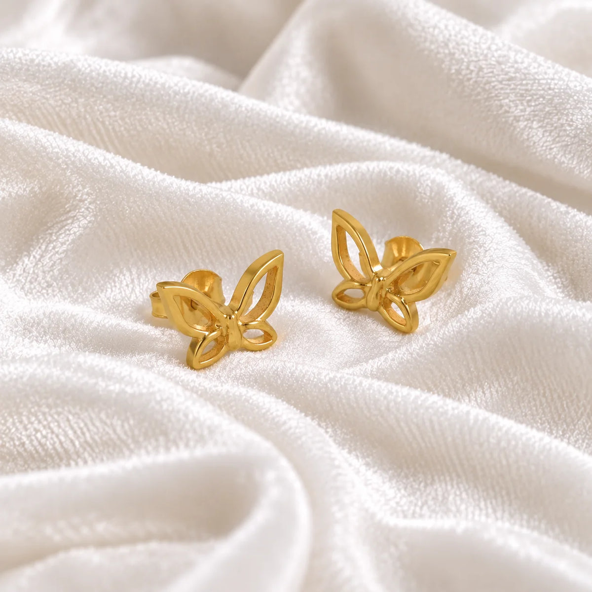 Butterfly_earrings_in_gold_plated_silver_in_a_stud_design_at_side_angle_view_on_soft_fabric_background