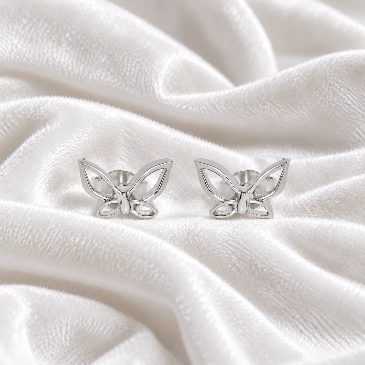 Butterfly_earrings_in_sterling_silver_in_a_stud_design_at_front_angle_view_on_soft_fabric_background