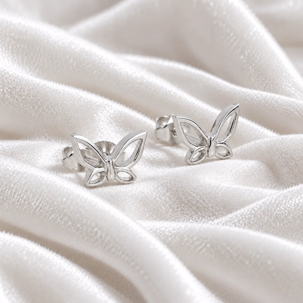 Butterfly_earrings_in_sterling_silver_in_a_stud_design_at_side_angle_view_on_soft_fabric_background