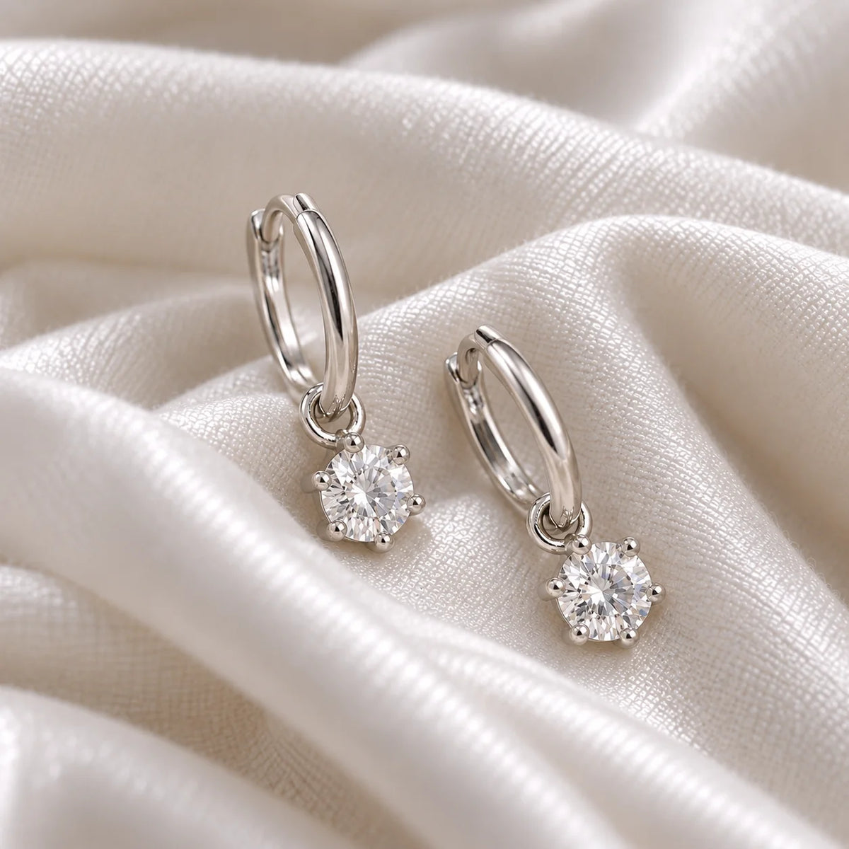 CZ_earrings_in_sterling_silver_with_a_hoop_drop_design_at_side_angle_view_on_soft_fabric_background