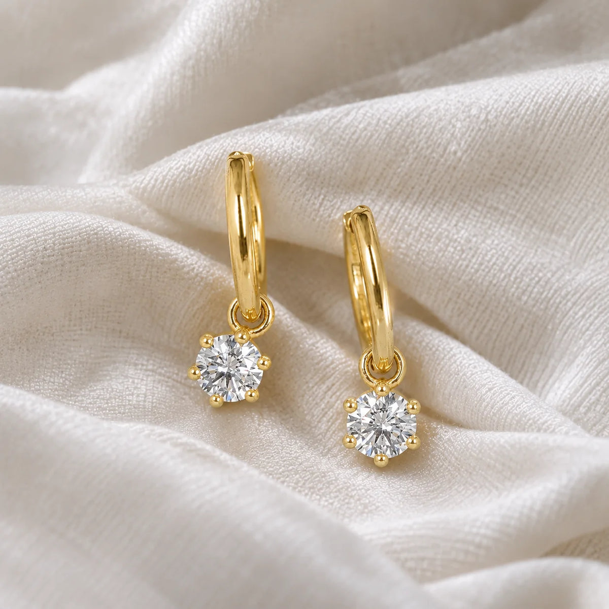 CZ_earrings_in_gold_plated_silver_with_a_hoop_drop_design_at_side_angle_view_on_soft_fabric_background