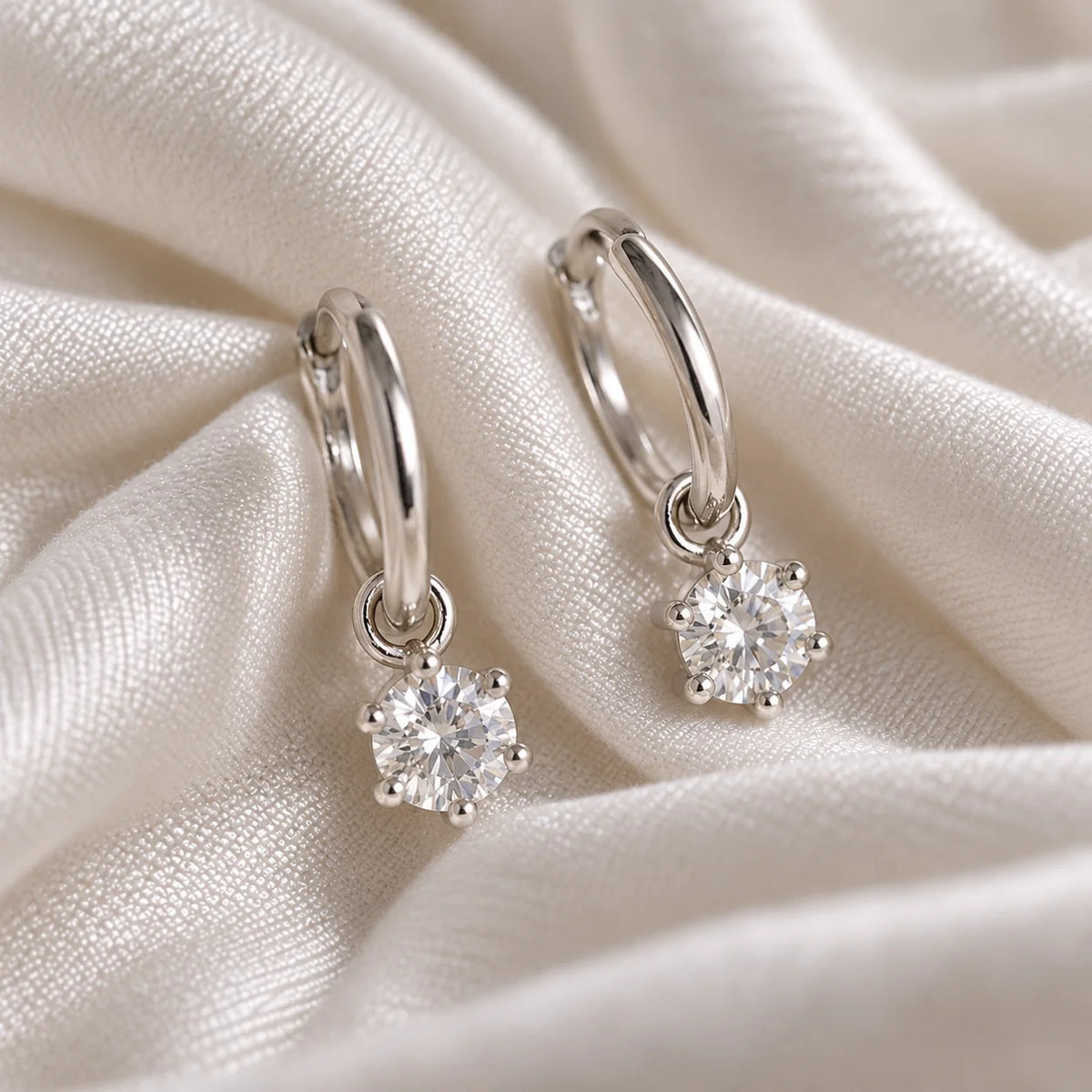CZ_earrings_in_sterling_silver_with_a_hoop_drop_design_at_front_angle_view_on_soft_fabric_background