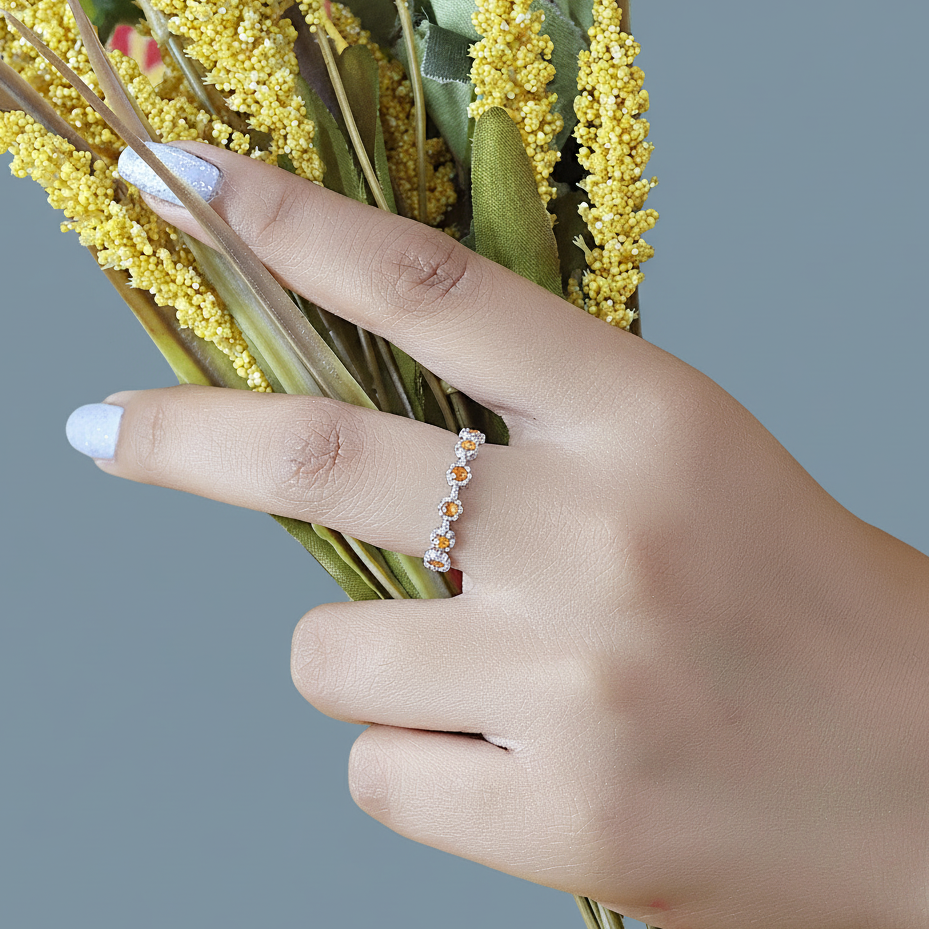 Carnelian ring with daisy flower shaped settings on a silver band shown at an angle on a swirling white velvet fabric background.