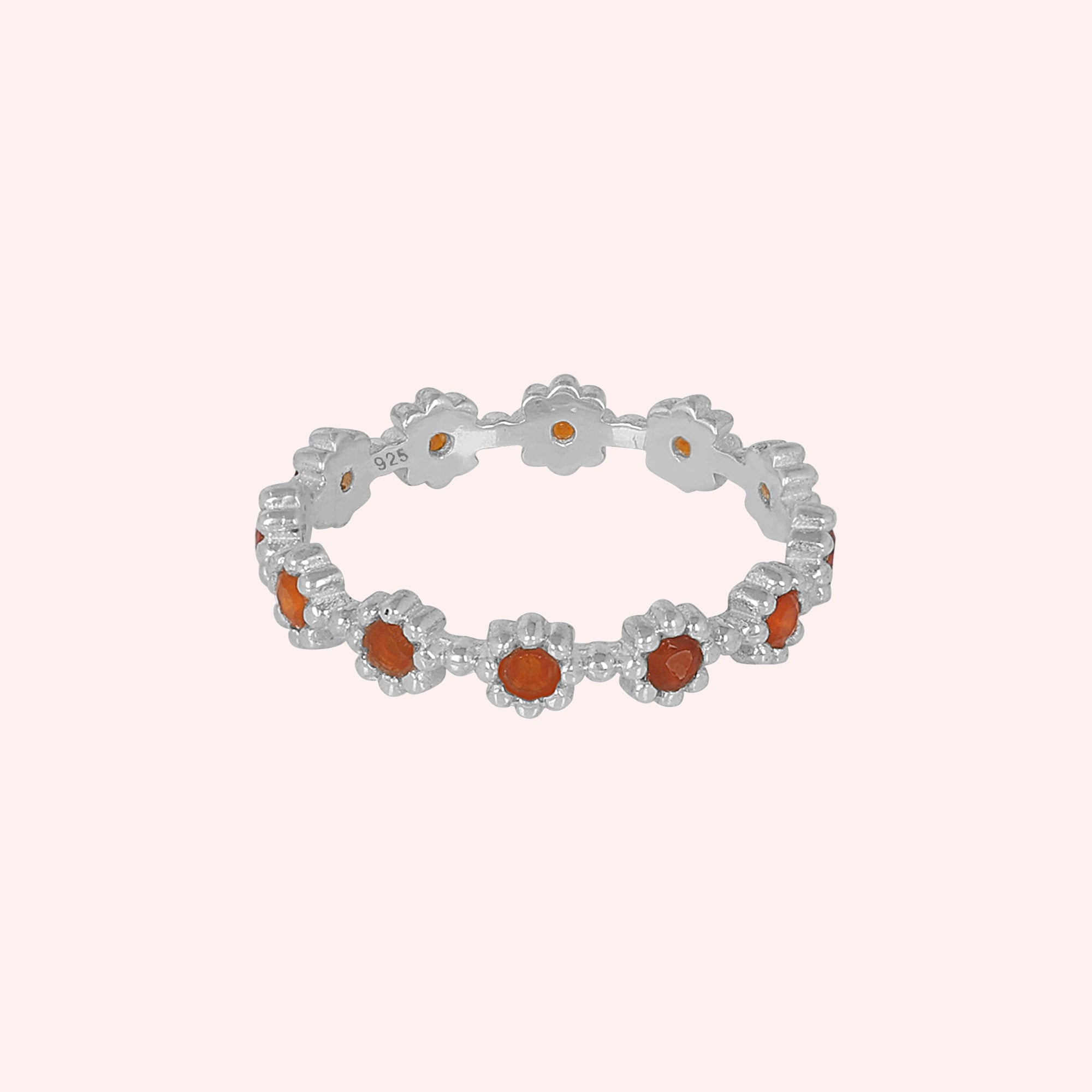 Carnelian ring with daisy flower settings on a thin silver carnelian ring band shown straight-on against a pale pink background.