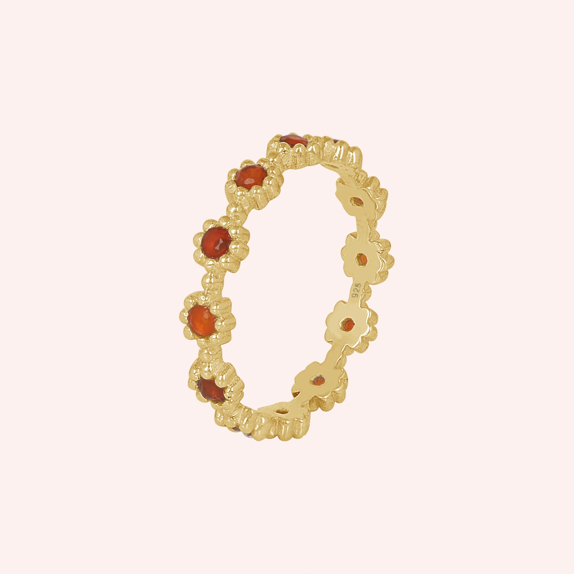 Carnelian ring with a gold vermeil finish and small daisy flower settings around the band shown at a slight angle on a pale pink background.