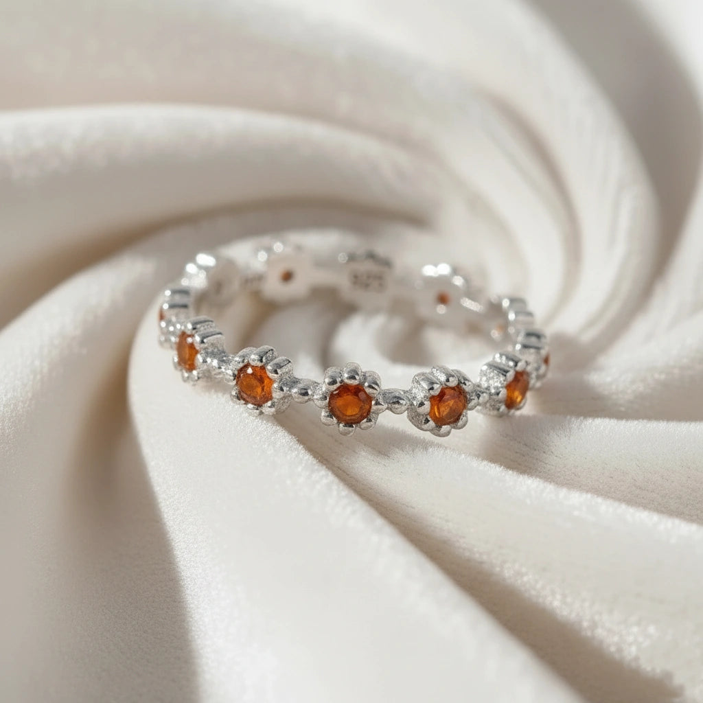 Carnelian ring with daisy flower shaped settings on a silver band shown at a slightly overhead angle on a swirling white velvet background.