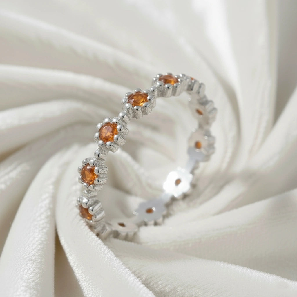 Carnelian ring with daisy flower shaped settings on a silver band shown at an angle on a swirling white velvet fabric background.