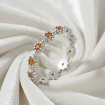 Carnelian ring with daisy flower shaped settings on a silver band shown at an angle on a swirling white velvet fabric background.