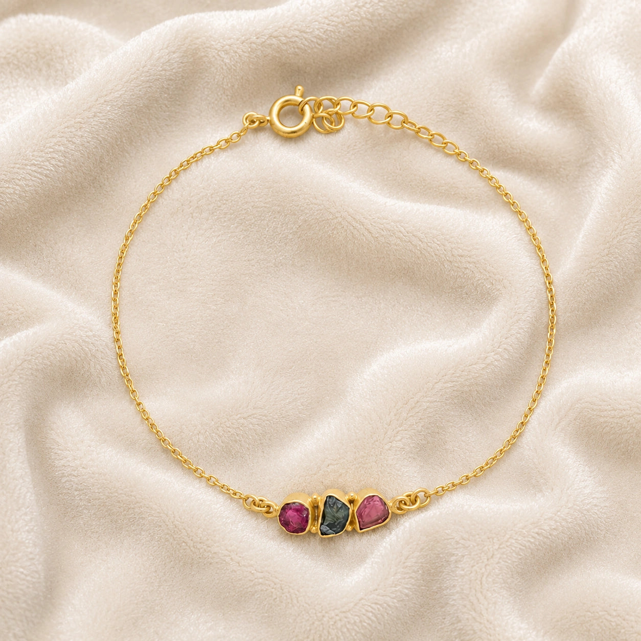 Chain_bracelet_in_gold_plated_silver_with_pink_and_green_tourmaline_stones_at_front_angle_view_on_soft_fabric_background