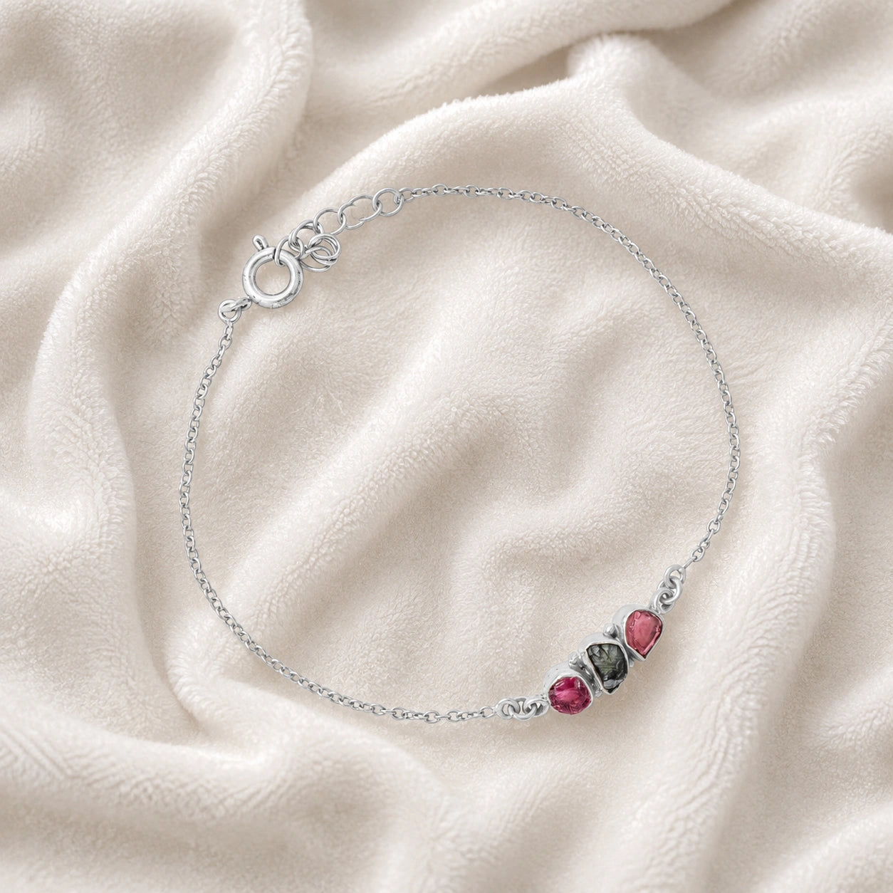 Chain_bracelet_in_sterling_silver_with_pink_and_green_tourmaline_stones_at_slight_angle_view_on_soft_fabric_background