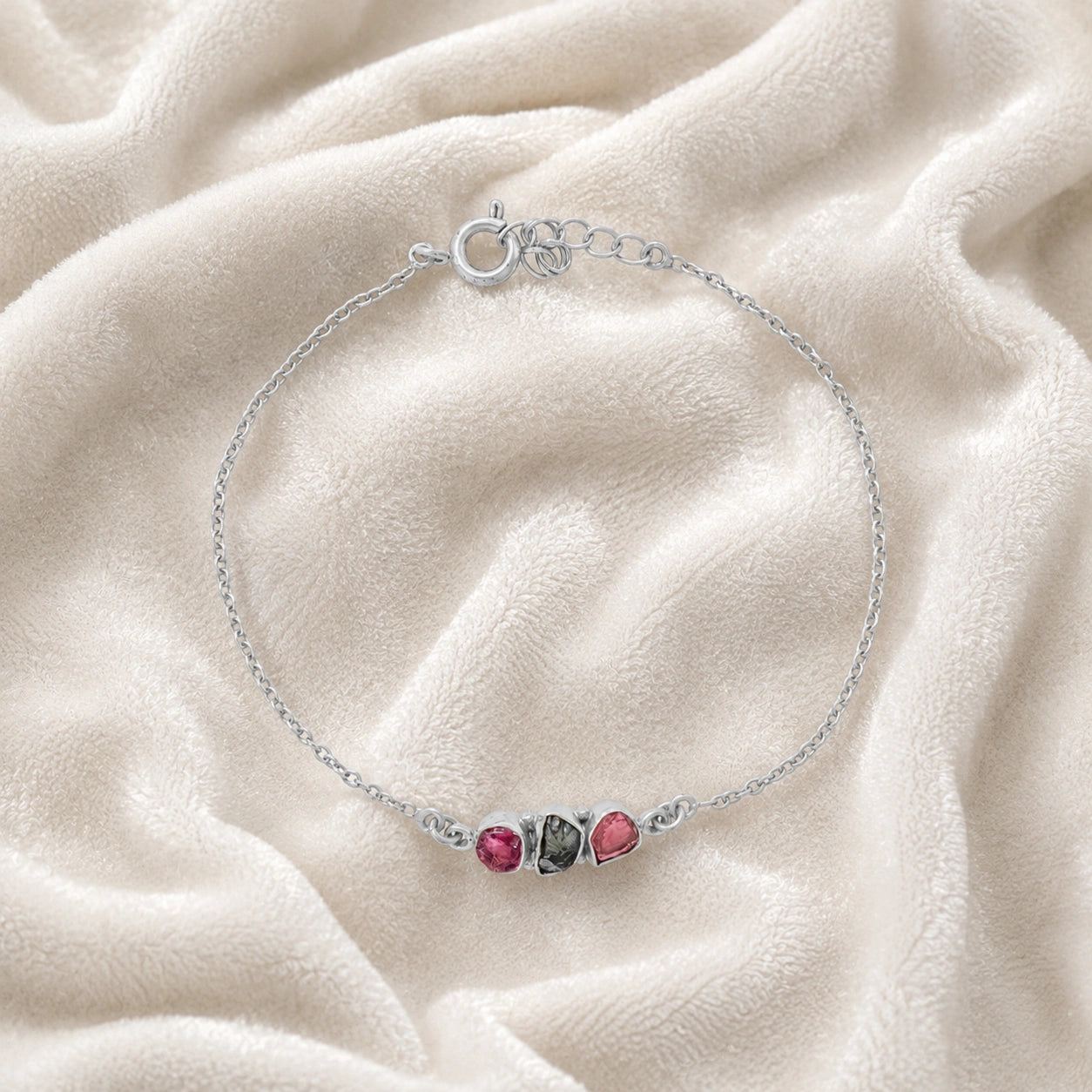 Chain_bracelet_in_sterling_silver_with_pink_and_green_tourmaline_stones_at_front_angle_view_on_soft_fabric_background