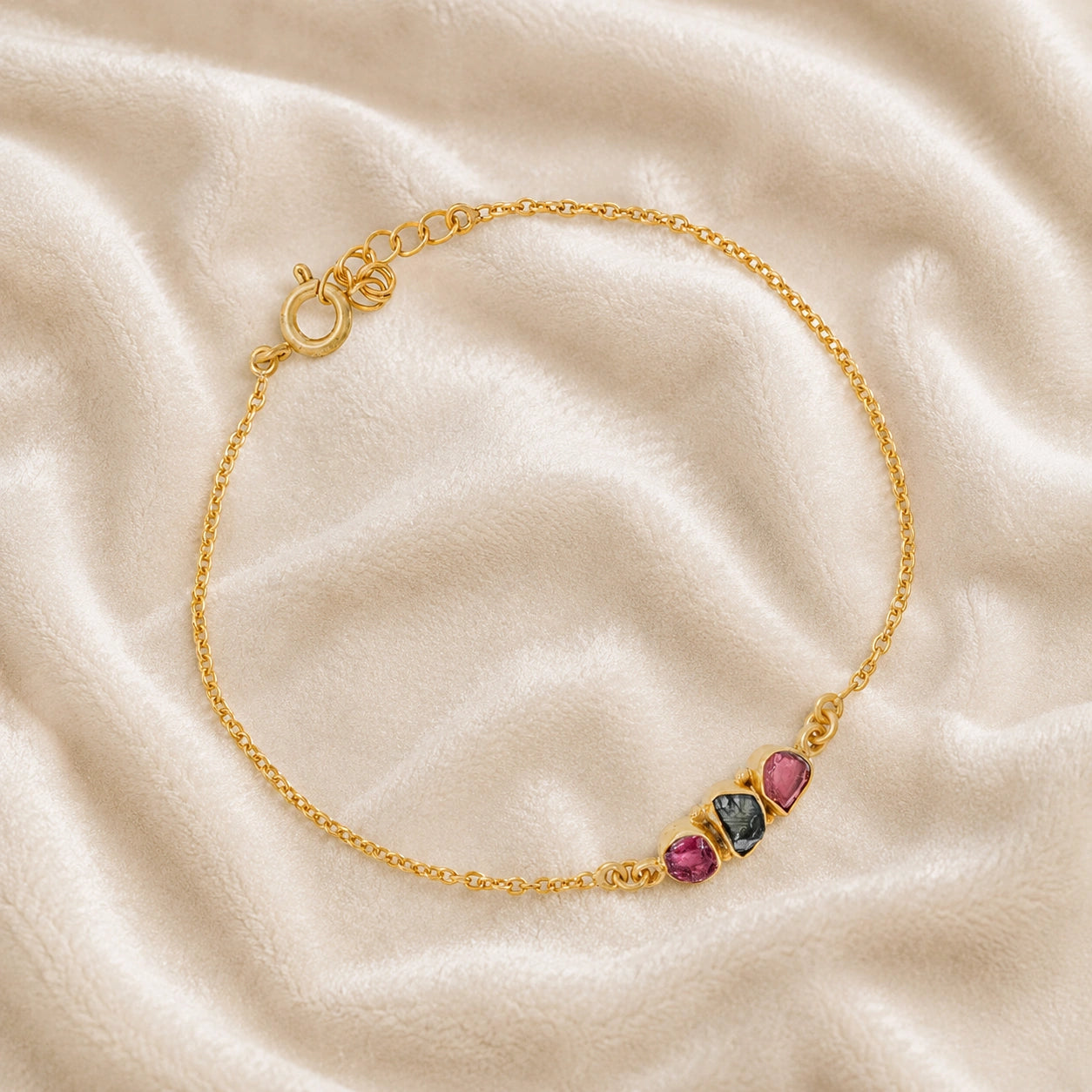 Chain_bracelet_in_gold_plated_silver_with_pink_and_green_tourmaline_stones_at_slight_angle_view_on_soft_fabric_background