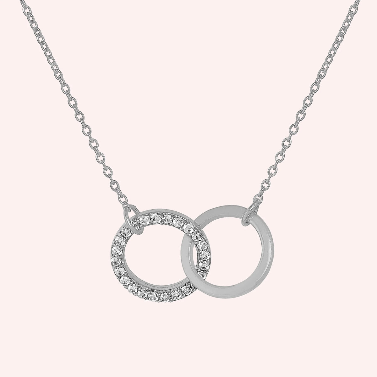 Charm_necklace_in_sterling_silver_with_interlock_circles_and_lab_grown_diamonds_at_front_angle_view_on_solid_pink_background
