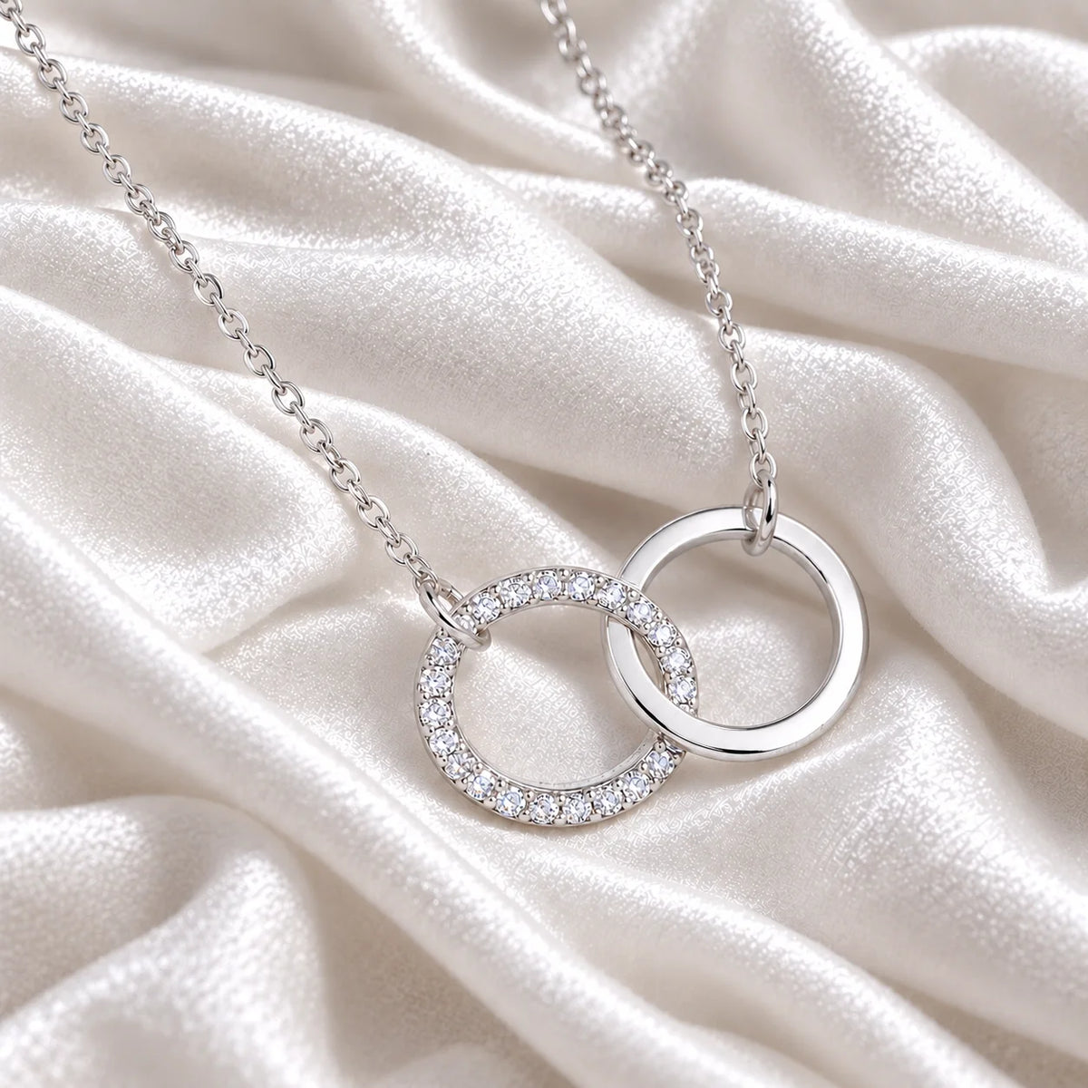 Charm_necklace_in_sterling_silver_with_interlock_circles_and_lab_grown_diamonds_at_side_angle_view_on_soft_fabric_background