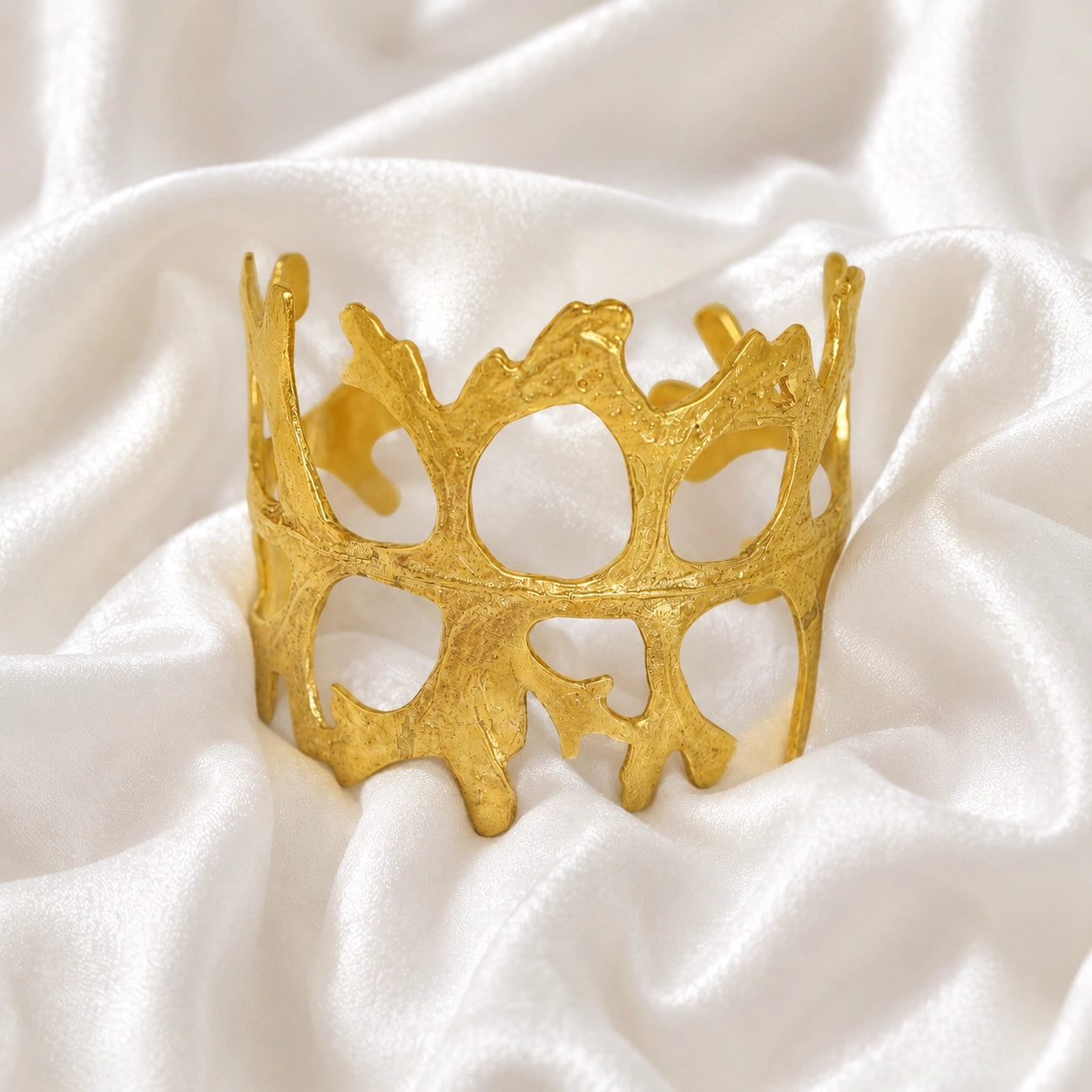 Chunky_bracelet_in_gold_plated_silver_showing_openwork_organic_adjustable_cuff_design_at_front_view_on_soft_fabric_background