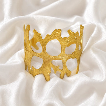 Chunky_bracelet_in_gold_plated_silver_showing_openwork_organic_adjustable_cuff_design_at_front_view_on_soft_fabric_background