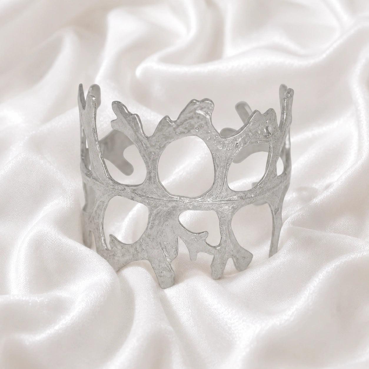 Chunky_bracelet_in_sterling_silver_showing_openwork_organic_adjustable_cuff_design_at_front_view_on_soft_fabric_background