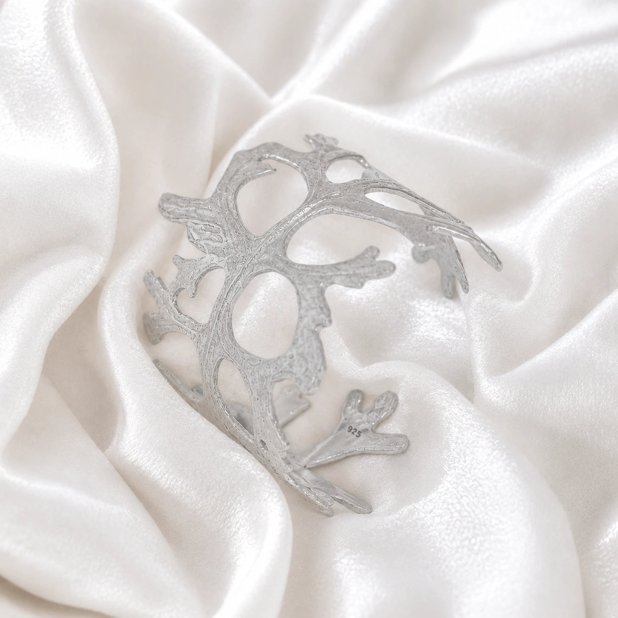 Chunky_bracelet_in_sterling_silver_showing_openwork_organic_adjustable_cuff_design_at_slight_view_on_soft_fabric_background