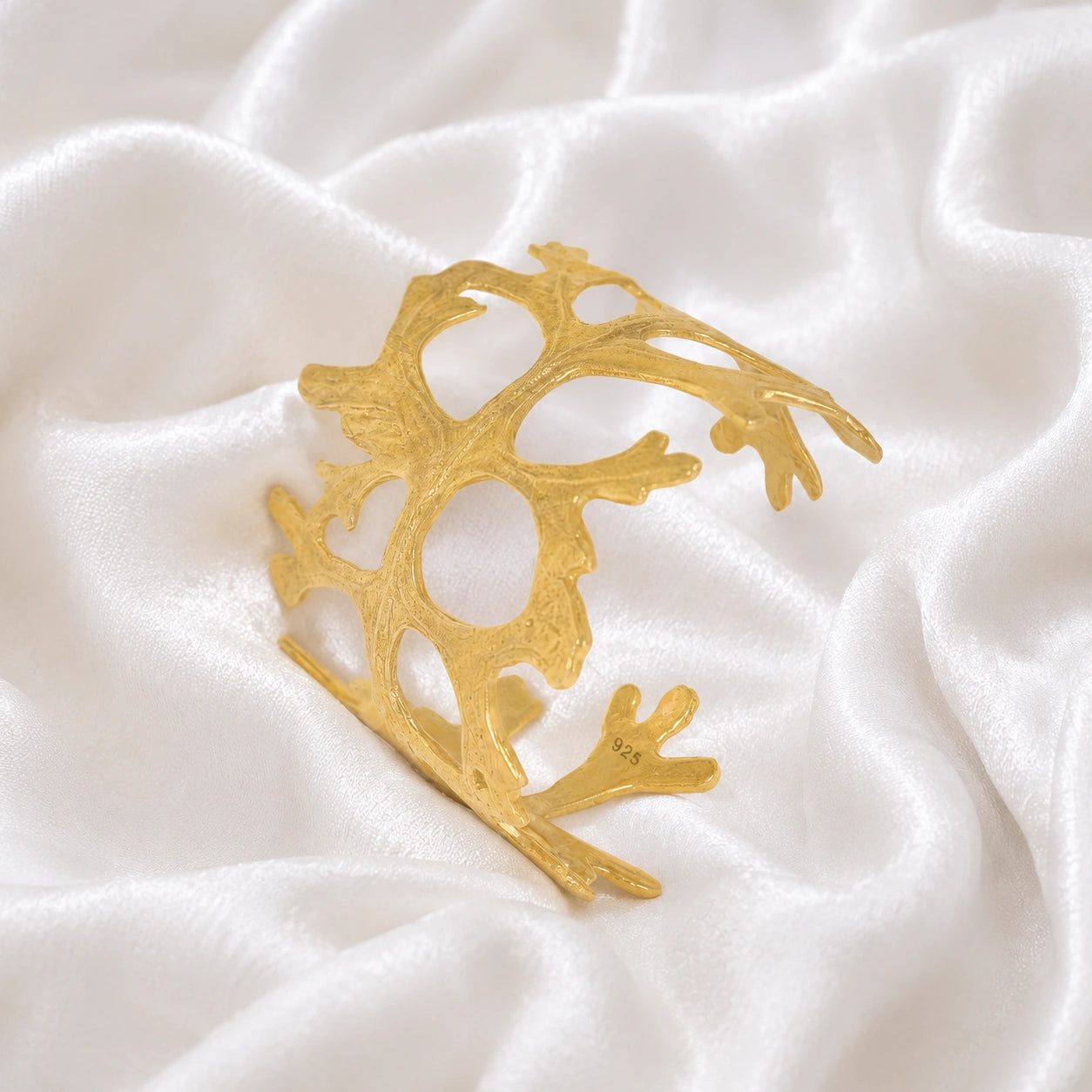 Chunky_bracelet_in_gold_plated_silver_showing_openwork_organic_adjustable_cuff_design_at_slight_view_on_soft_fabric_background