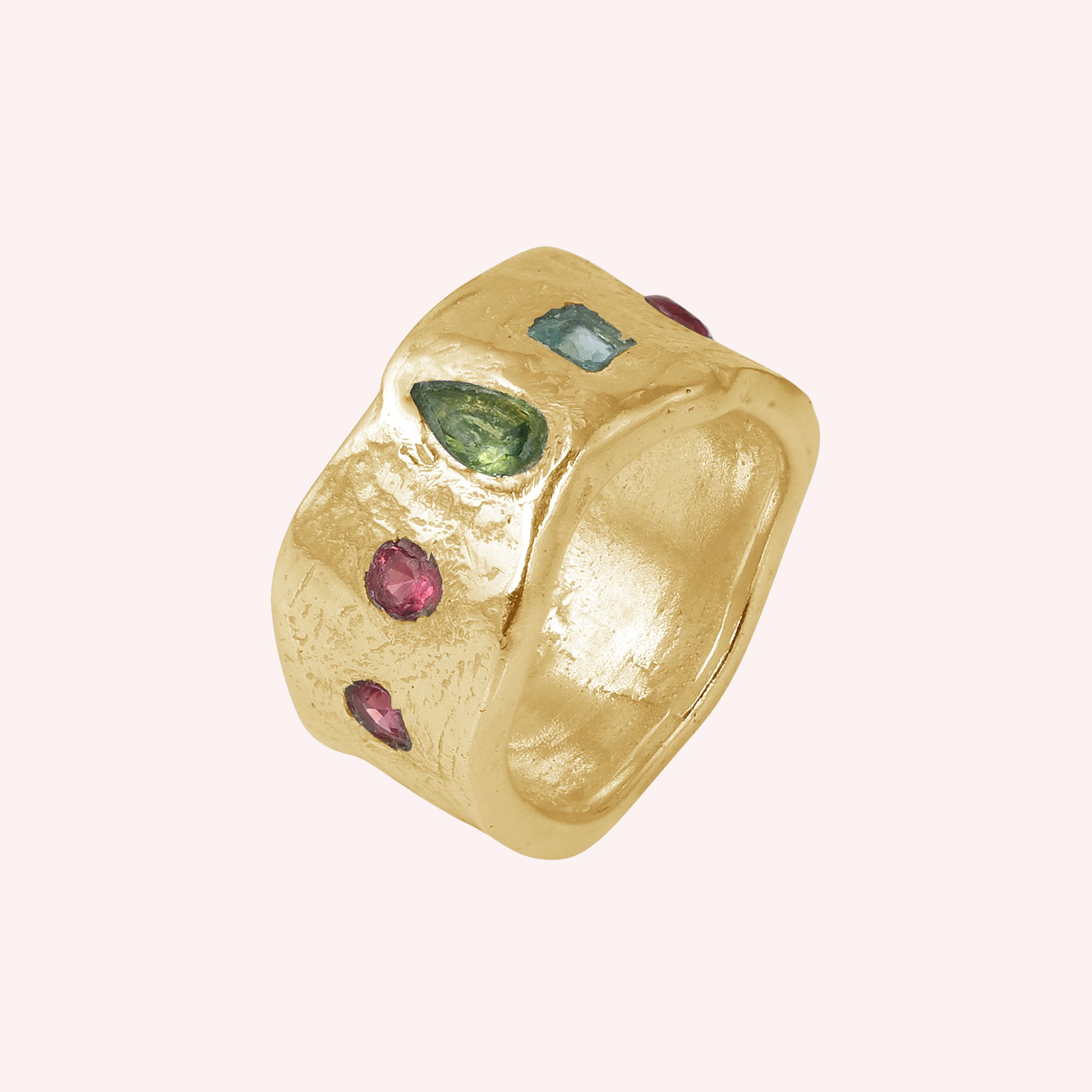 Chunky_ring_in_gold_plated_silver_at_slight_angle_with_pink_tourmaline_peridot_and_blue_topaz_stones_on_a_solid_pink_background