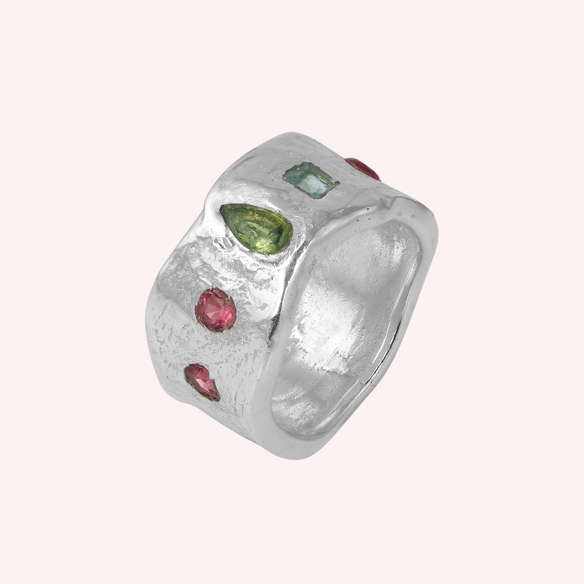 Chunky_ring_in_sterling_silver_at_slight_angle_with_pink_tourmaline_peridot_and_blue_topaz_stones_on_a_solid_pink_background