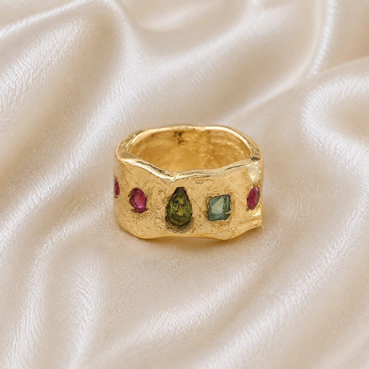 Chunky_ring_in_gold_plated_silver_at_front_angle_with_pink_tourmaline_peridot_and_blue_topaz_stones_on_a_soft_fabric_background