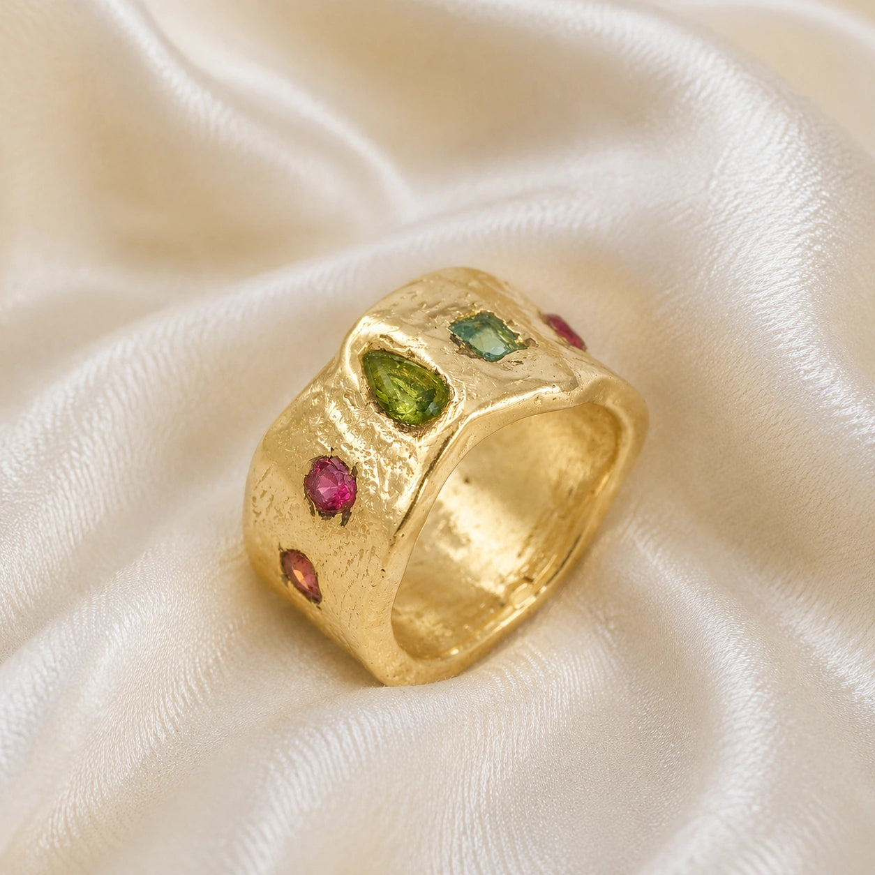 Chunky_ring_in_gold_plated_silver_at_slight_angle_with_pink_tourmaline_peridot_and_blue_topaz_stones_on_a_soft_fabric_background