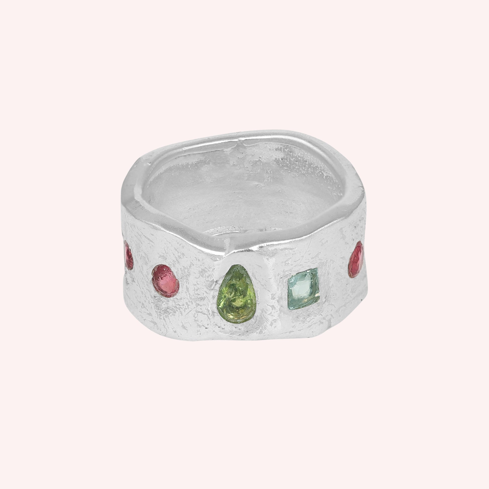 Chunky_ring_in_sterling_silver_at_front_angle_with_pink_tourmaline_peridot_and_blue_topaz_stones_on_a_solid_pink_background