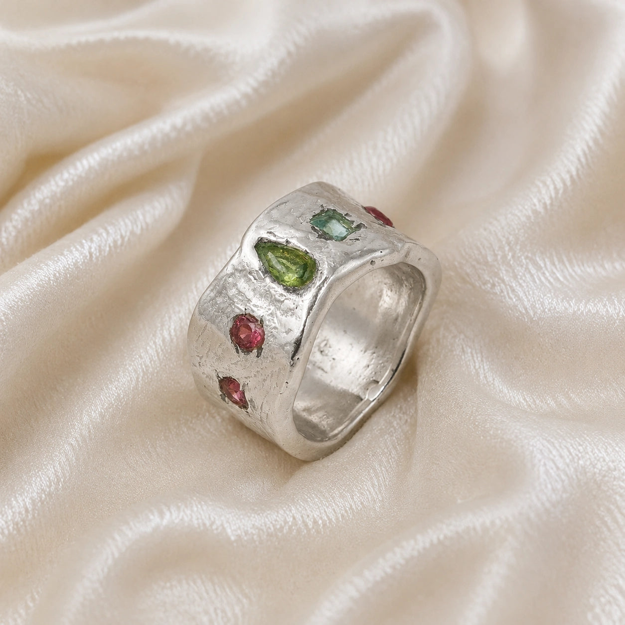 Chunky_ring_in_sterling_silver_at_slight_angle_with_pink_tourmaline_peridot_and_blue_topaz_stones_on_a_soft_fabric_background
