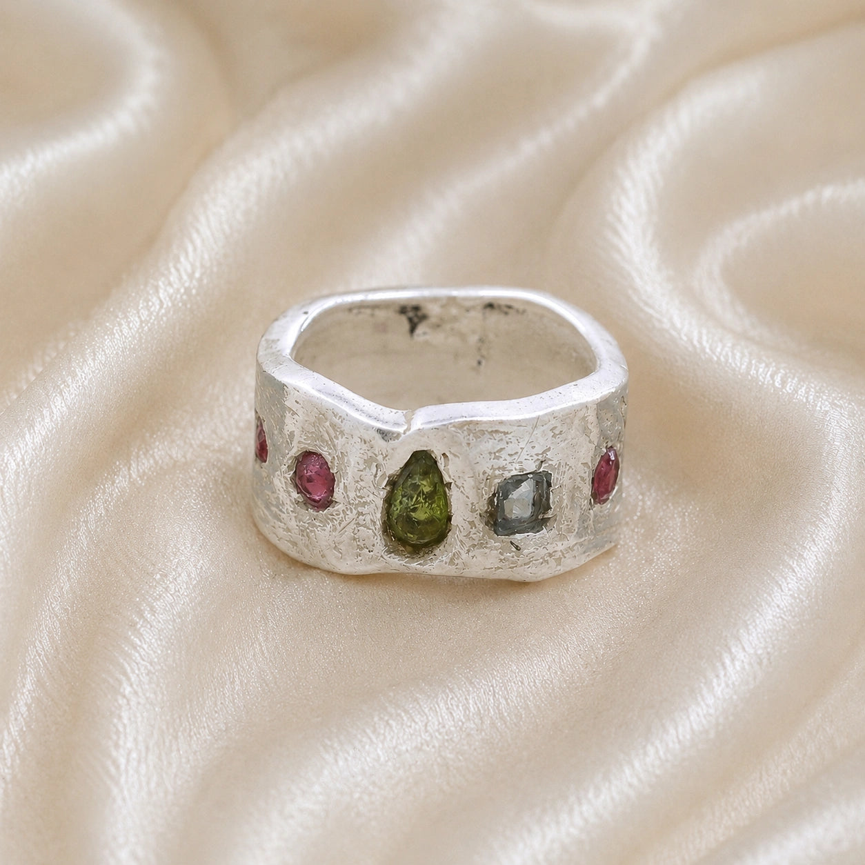Chunky_ring_in_sterling_silver_at_front_angle_with_pink_tourmaline_peridot_and_blue_topaz_stones_on_a_soft_fabric_background