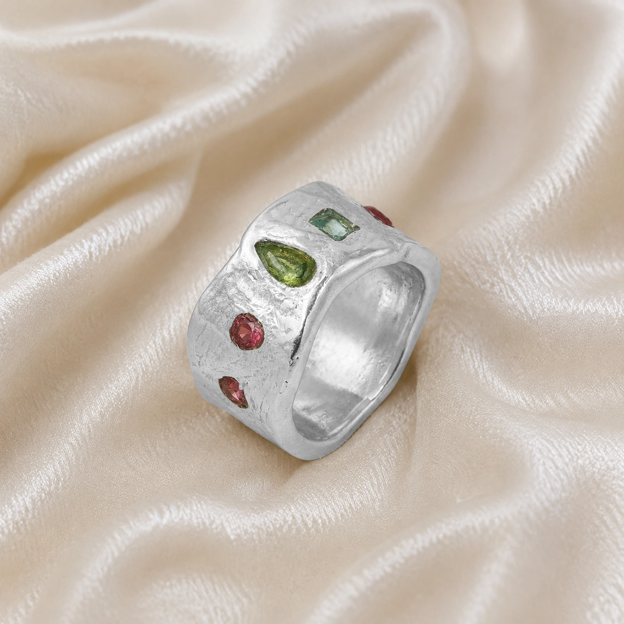 Chunky_ring_in_sterling_silver_at_slight_angle_with_pink_tourmaline_peridot_and_blue_topaz_stones_on_a_soft_fabric_background