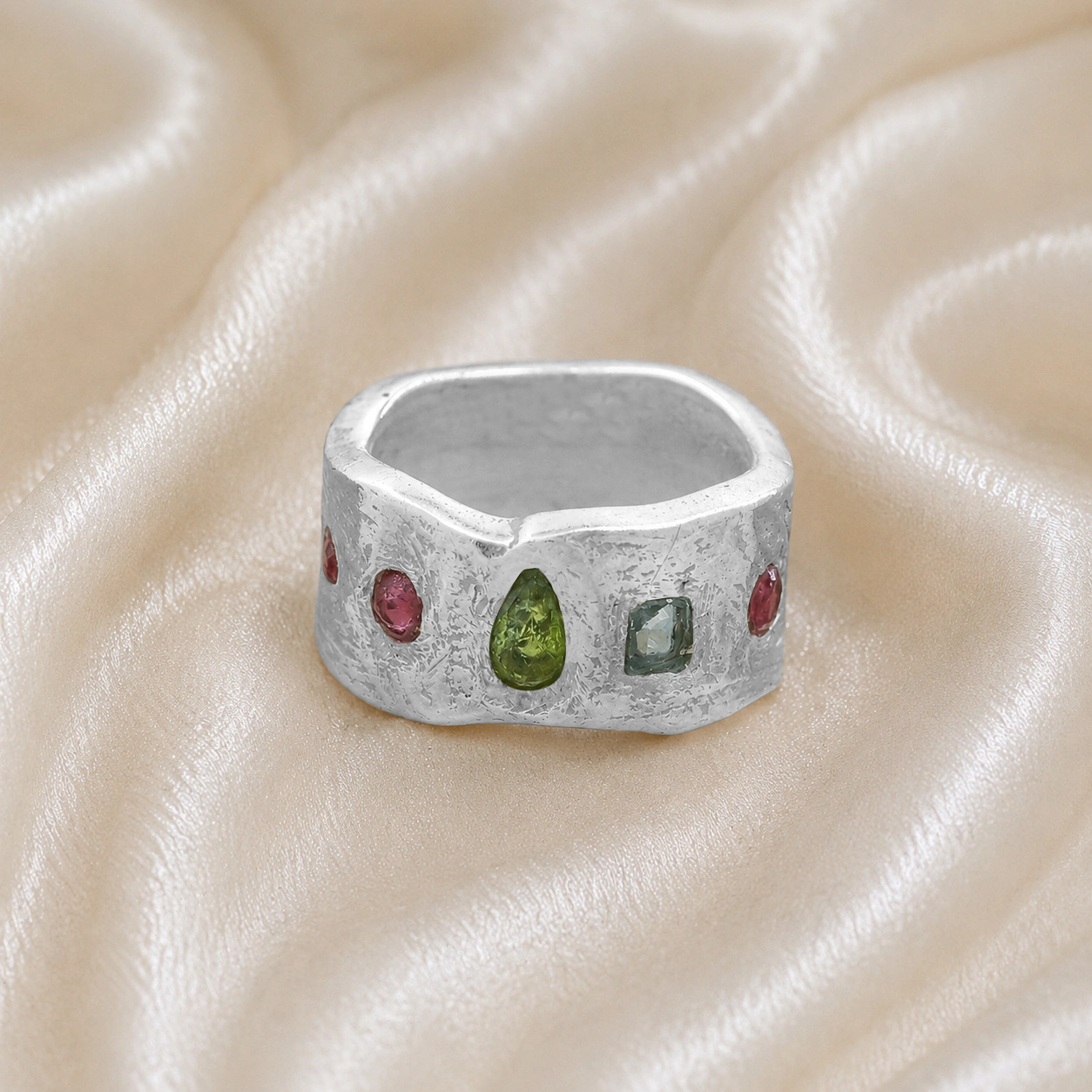 Chunky_ring_in_sterling_silver_at_front_angle_with_pink_tourmaline_peridot_and_blue_topaz_stones_on_a_soft_fabric_background