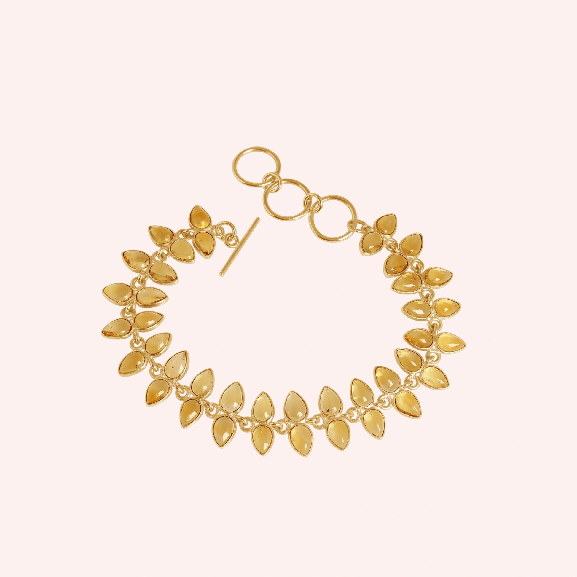 Citrine_bracelet_with_leaf_shaped_citrine_stones_in_gold_plated_silver_at_front_angle_view_on_solid_pink_background
