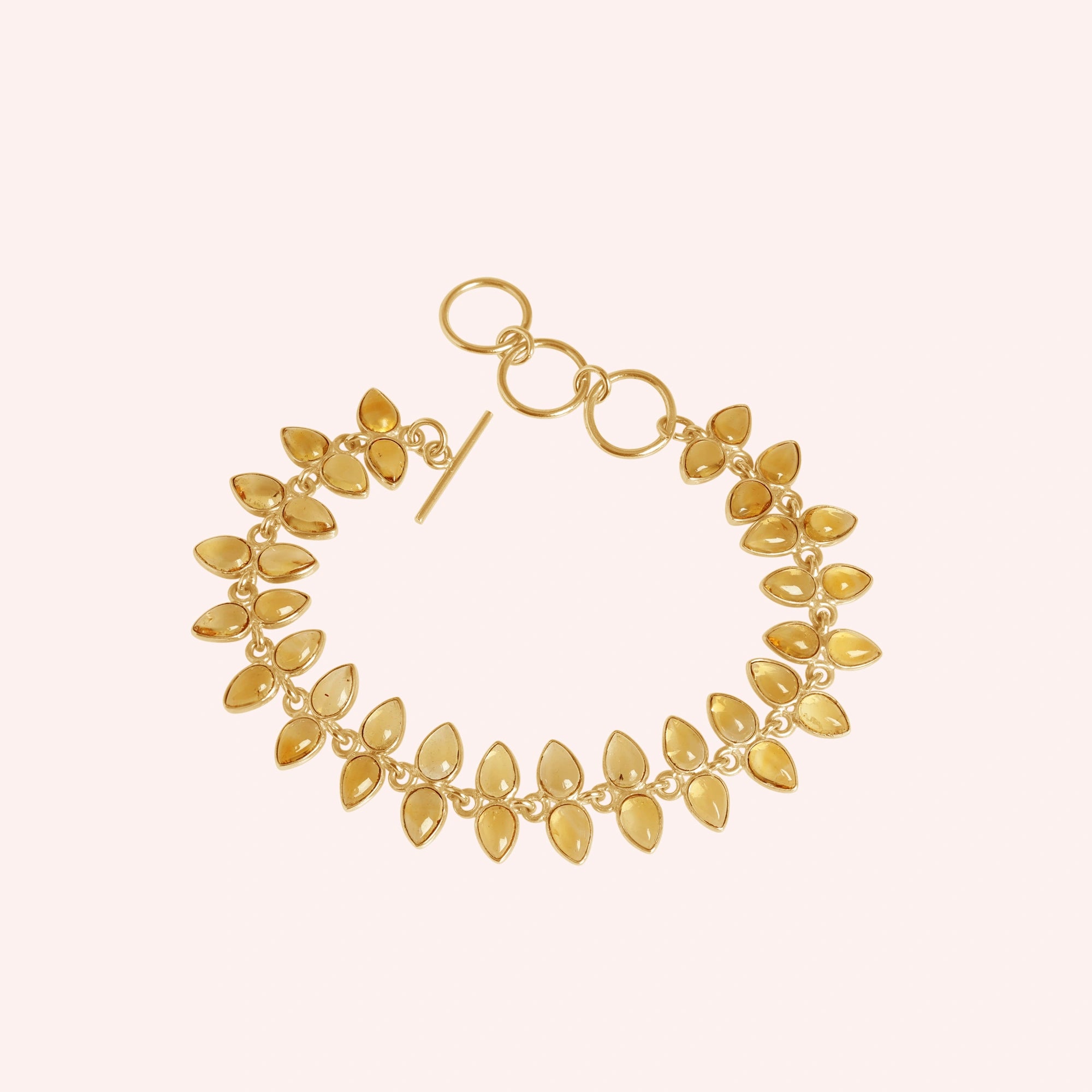 Citrine_bracelet_with_leaf_shaped_citrine_stones_in_gold_plated_silver_at_front_angle_view_on_solid_pink_background