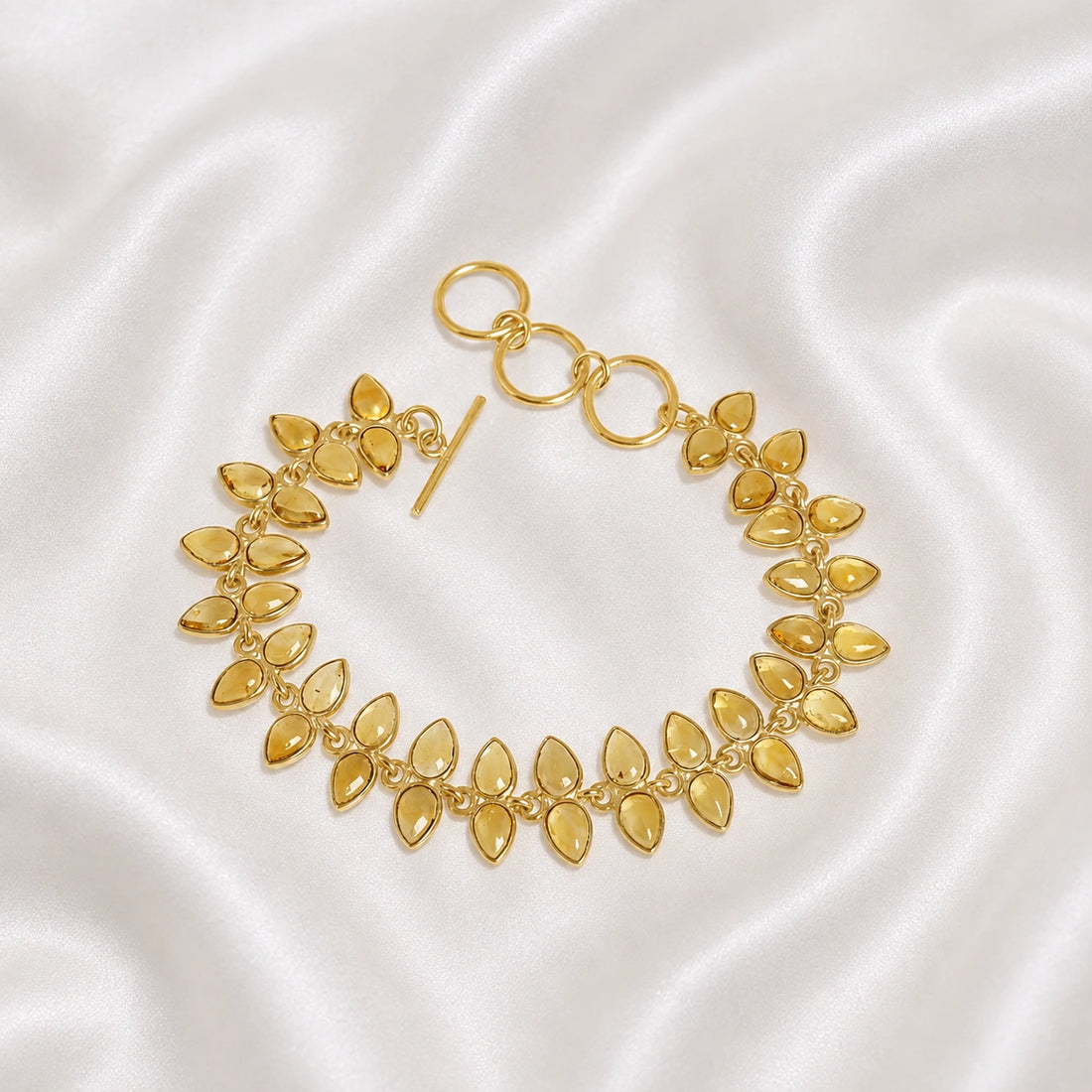 Citrine_bracelet_with_leaf_shaped_citrine_stones_in_gold_plated_silver_at_front_angle_view_on_soft_fabric_background