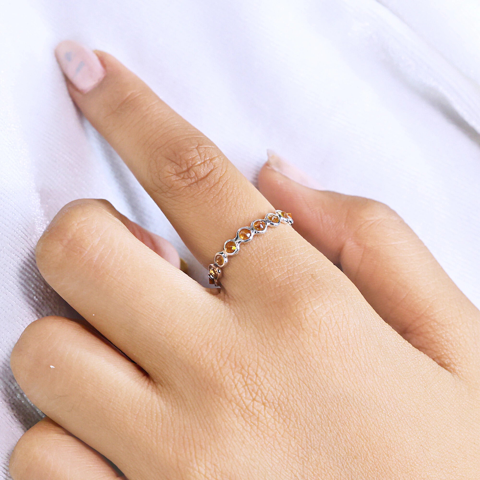 Angled close up shot of a hand wearing a sterling silver citrine ring on a white cloth with round cut yellow citrine stones