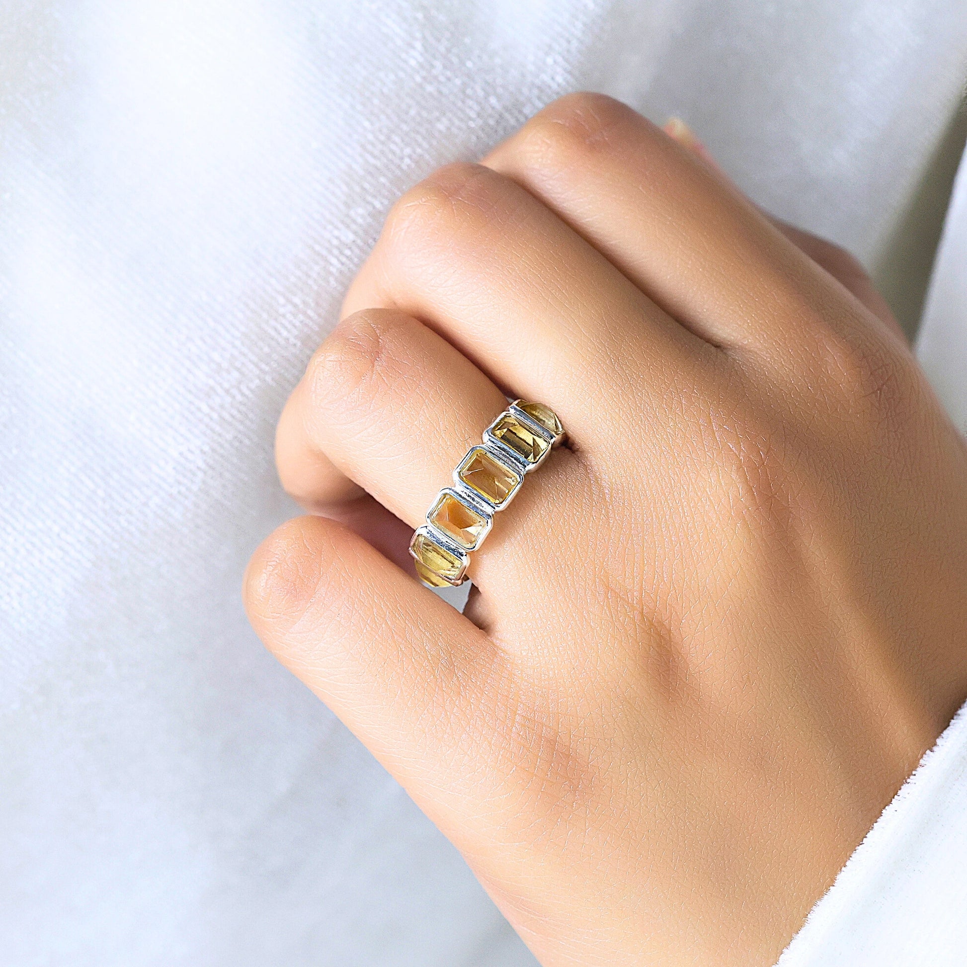 Angled shot of a hand wearing a sterling silver citrine ring on a white shirt background showcasing rectangular citrine stones.