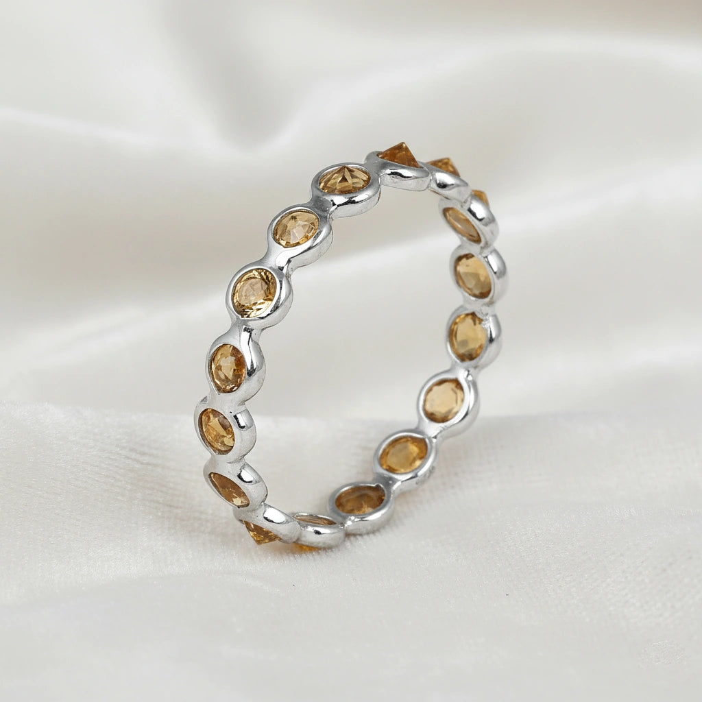 Angled close up shot of a sterling silver citrine ring on a white velvet background with round cut yellow citrine stones