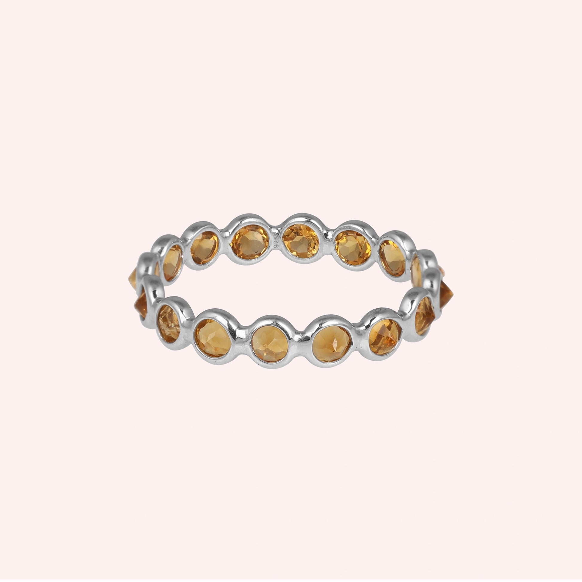 Horizontal shot of a sterling silver citrine ring on a light pink background showcasing round cut yellow citrine stones