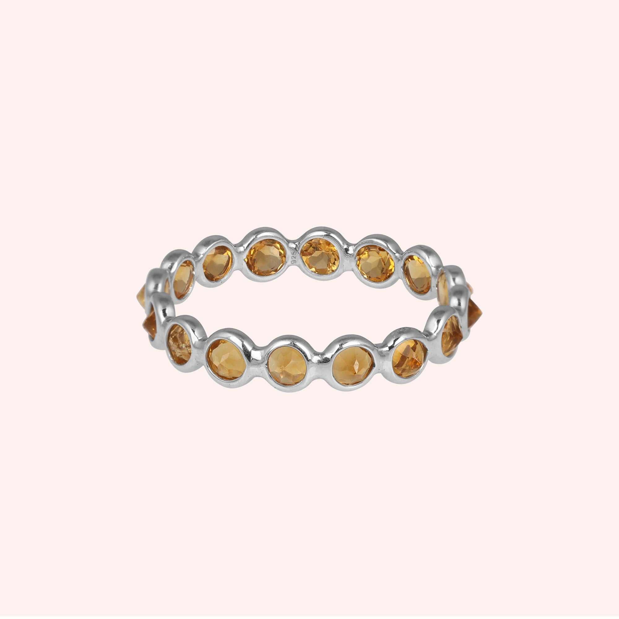 Horizontal shot of a sterling silver citrine ring on a light pink background showcasing round cut yellow citrine stones