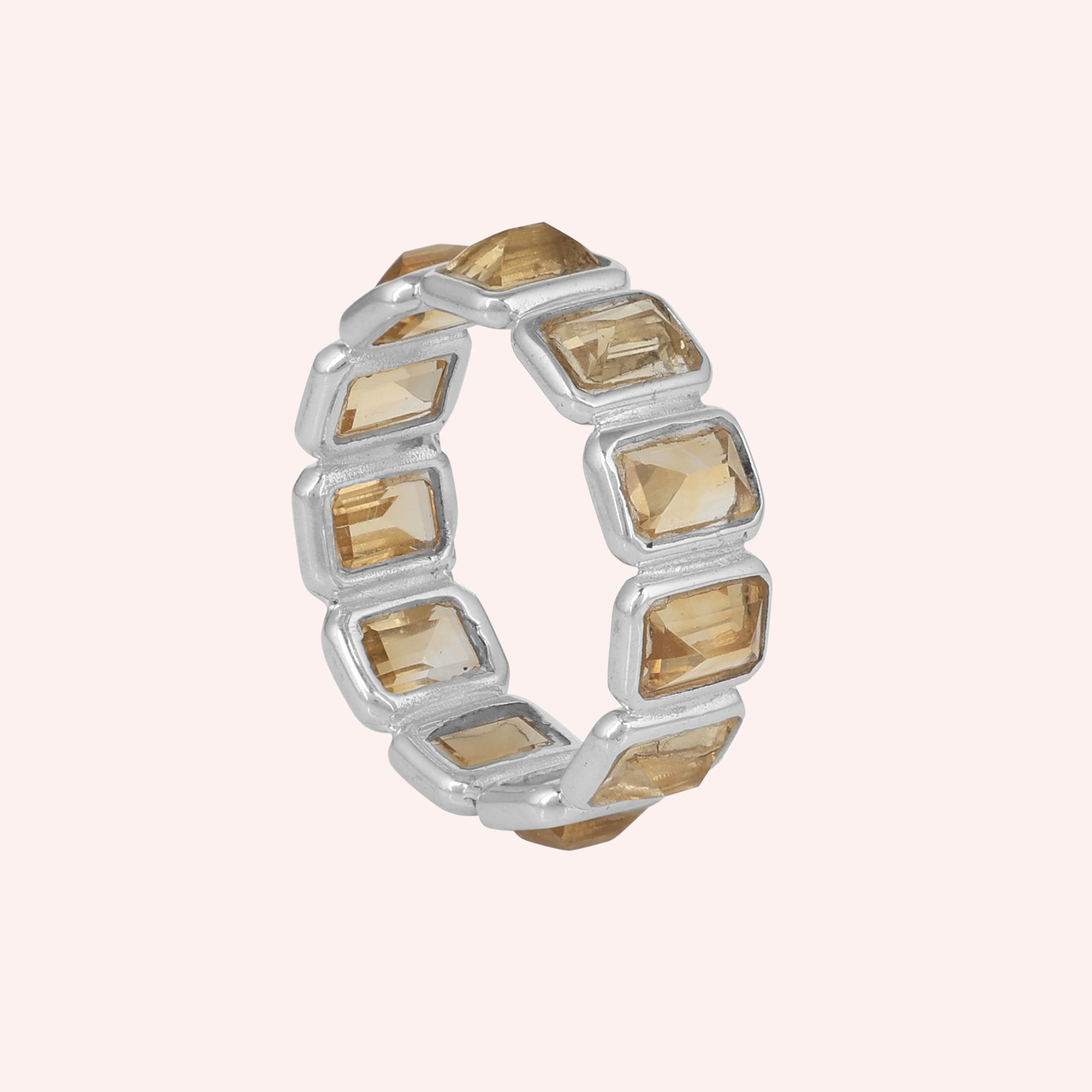 Angled shot of a sterling silver citrine ring on a light pink background showcasing rectangular citrine stones in a silver setting.