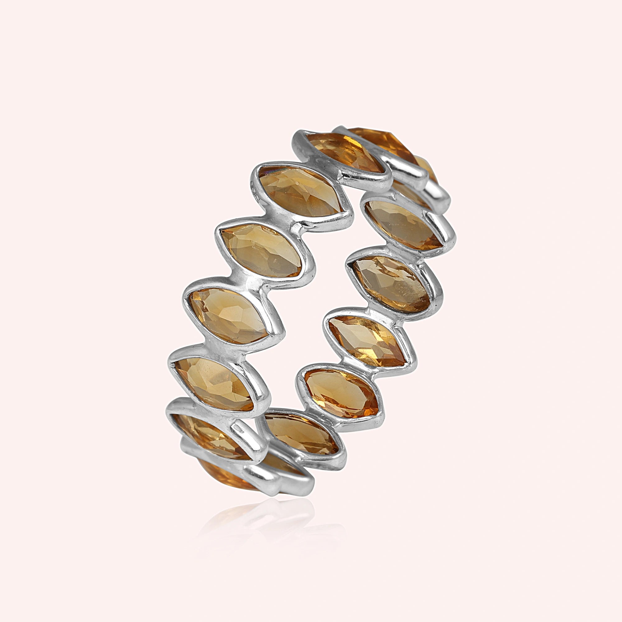 Sterling silver eternity ring featuring marquise citrine stones on a light pink background angled for visual depth.