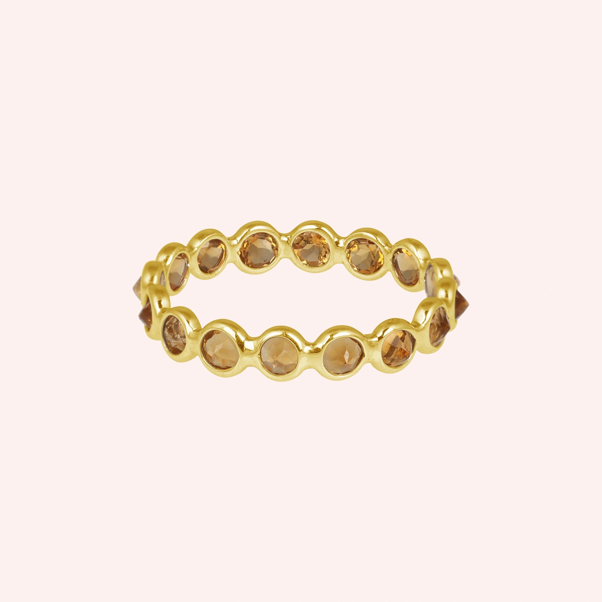Horizontal shot of a gold-plated sterling silver citrine ring on a light pink background with round cut yellow citrine stones