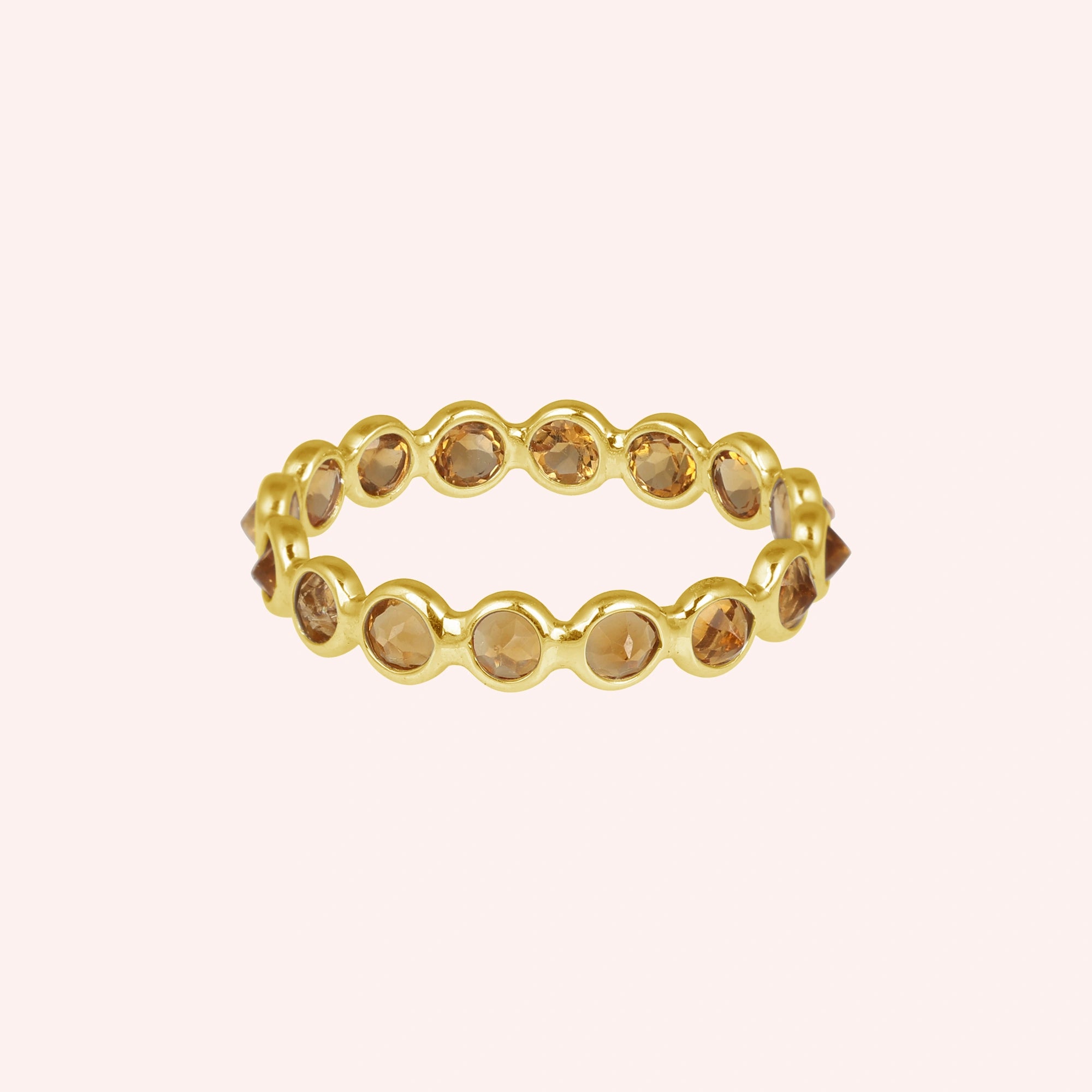 Horizontal shot of a gold-plated sterling silver citrine ring on a light pink background with round cut yellow citrine stones
