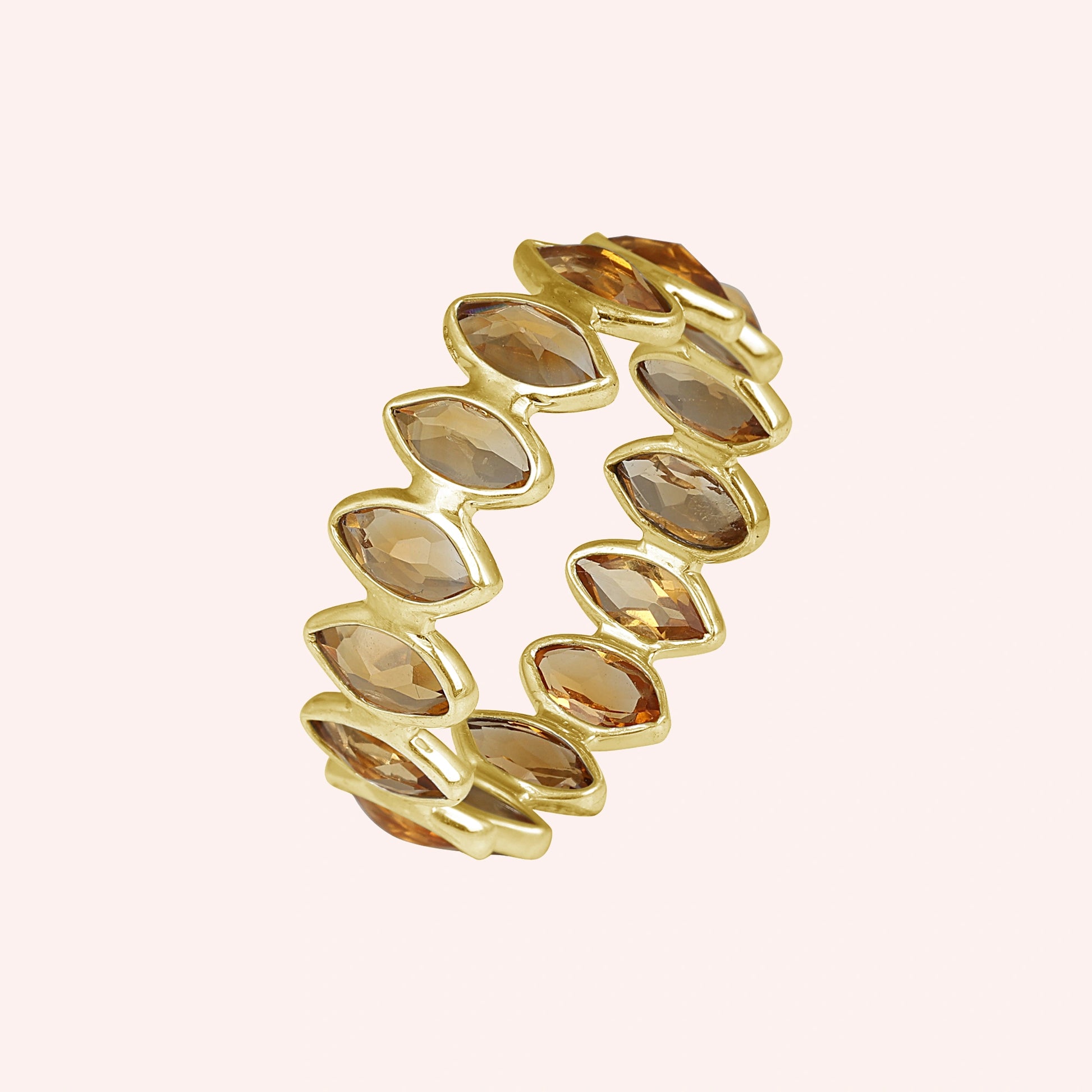 Gold vermeil citrine eternity ring featuring beautiful marquise stones on a light pink background angled for visual depth.