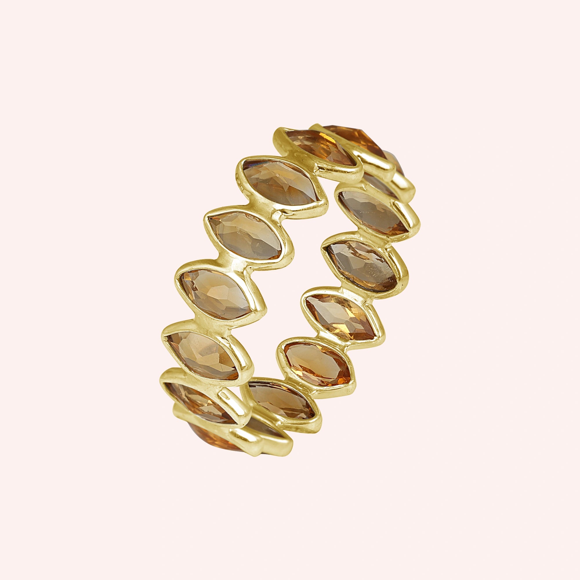 Gold vermeil citrine eternity ring featuring beautiful marquise stones on a light pink background angled for visual depth.