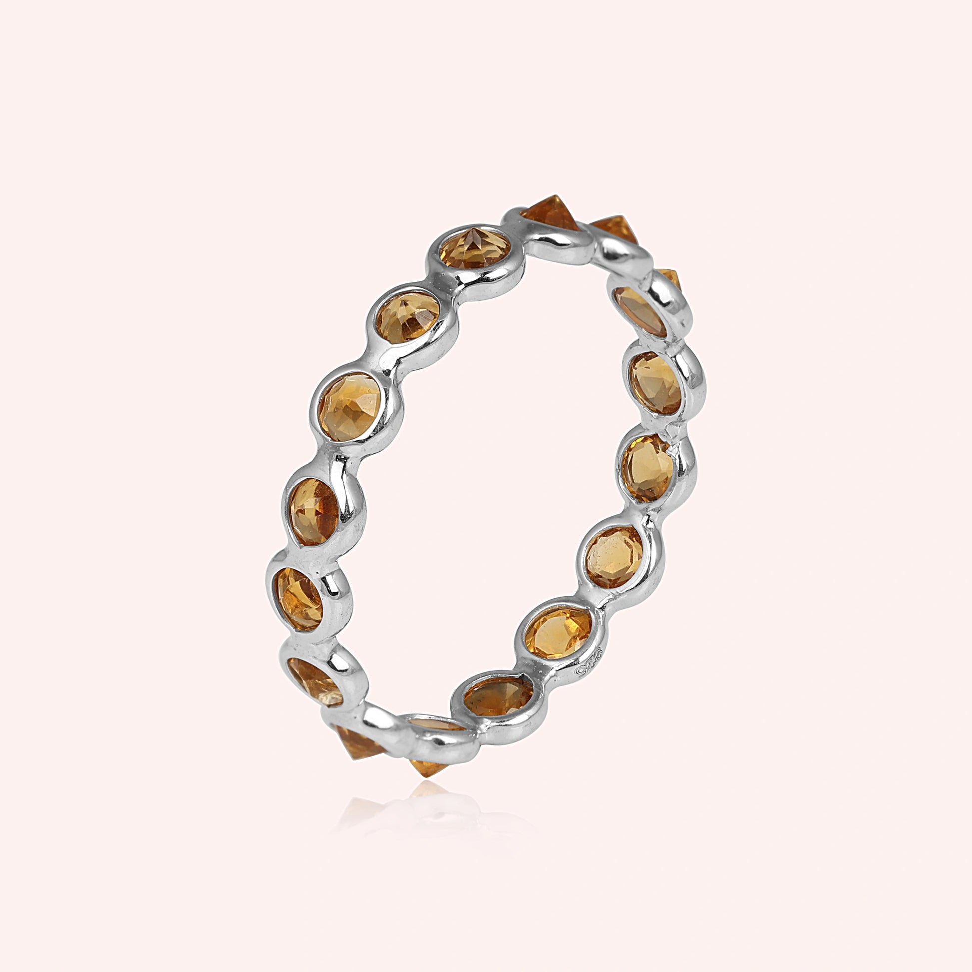 Angled close up shot of a sterling silver citrine ring on a light pink background with round cut yellow citrine stones